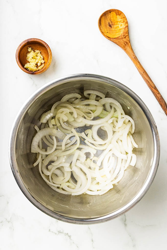 overhead view of instant pot with onions with garlic and wooden spoon on side