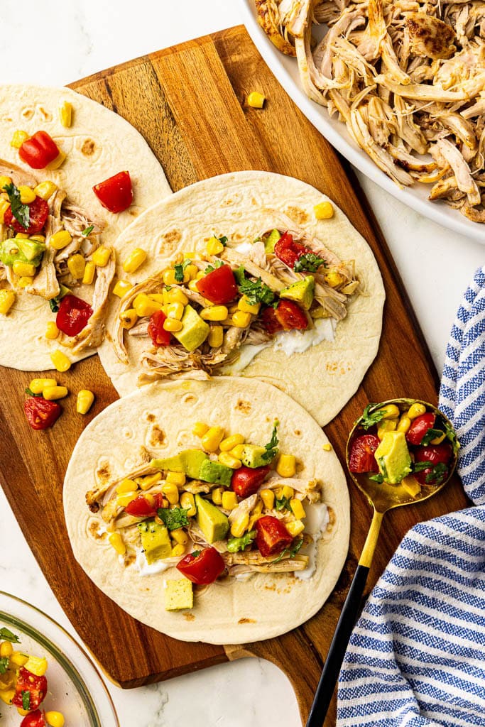 wooden cutting board with 3 chicken and salsa filled tortillas with spoon, with shredded chicken and salsa on side