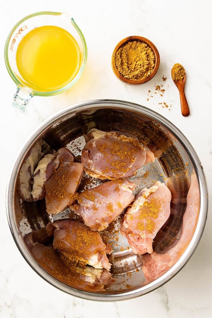 instant pot with seasoned chicken thighs with containers of chicken broth and taco seasoning on side