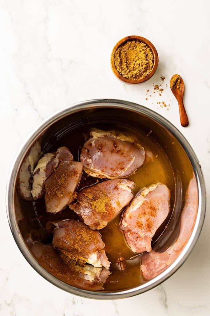 instant pot containing seasoned chicken thighs with chicken broth, with container of taco seasoning on side
