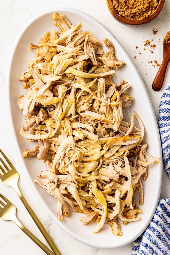 white platter of shredded chicken thighs with 2 forks and taco seasoning on side