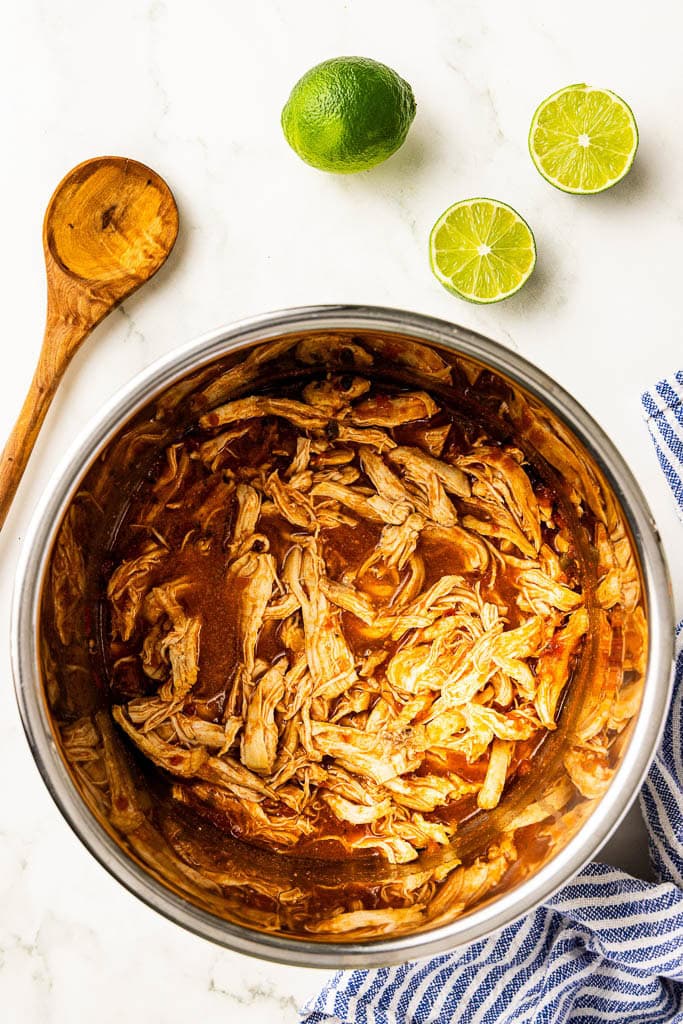 overhead view of Mexican chicken in instant pot with wooden spoon, whole lime, 2 lime halves and wooden spoon on side