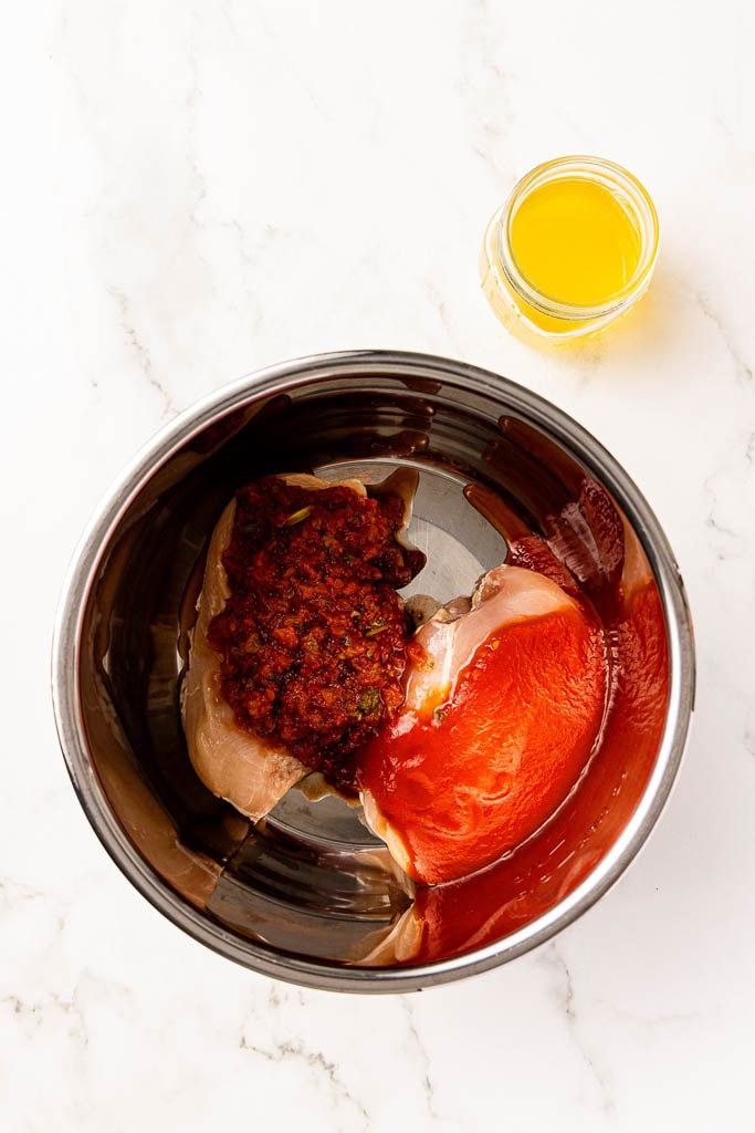 instant pot with 2 chicken breasts, salsa and tomato sauce with container of chicken broth on side