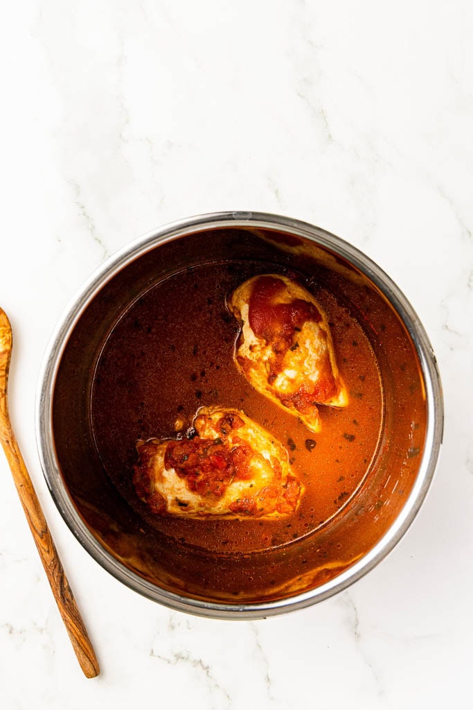 instant pot with cooked chicken breasts with wooden spoon on side