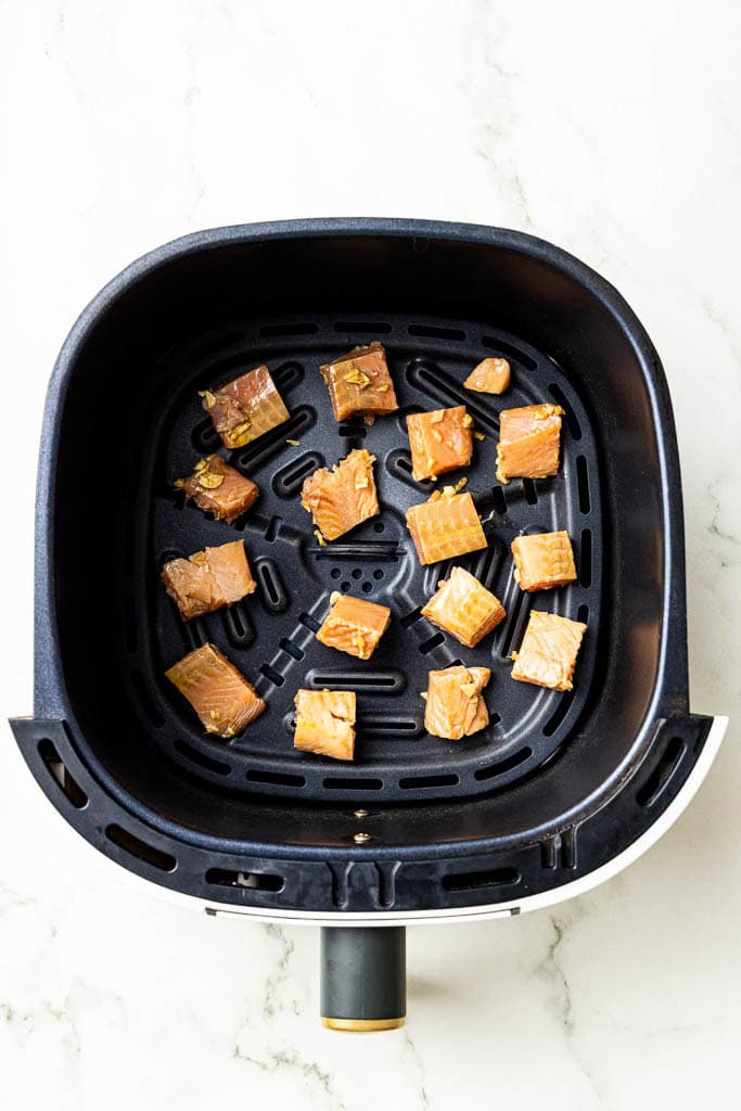 overhead view of uncooked cubed and marinated salmon bites in black air fryer