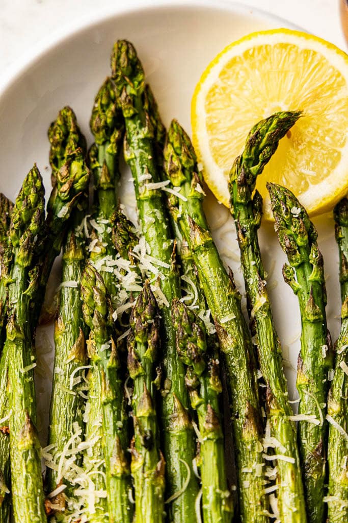 closeup of baked asparagus on white serving platter with lemon slice