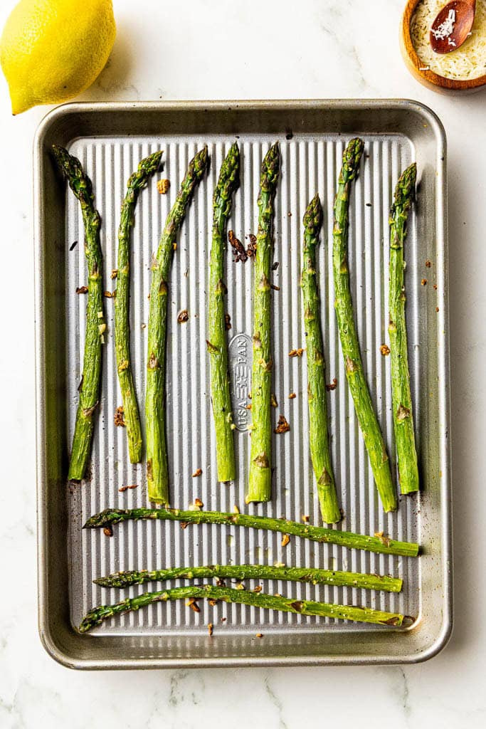 baking sheet with baked asparagus surrounded by a lemon and Parmesan cheese