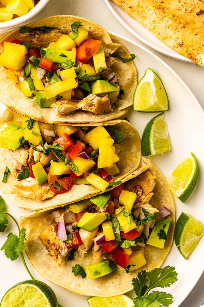 overhead view with dinner plate containing 3 filled tortillas with lime wedges, with plate of mahi mahi on side