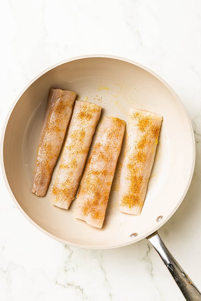 oiled skillet with 4 seasoned mahi mahi fillets