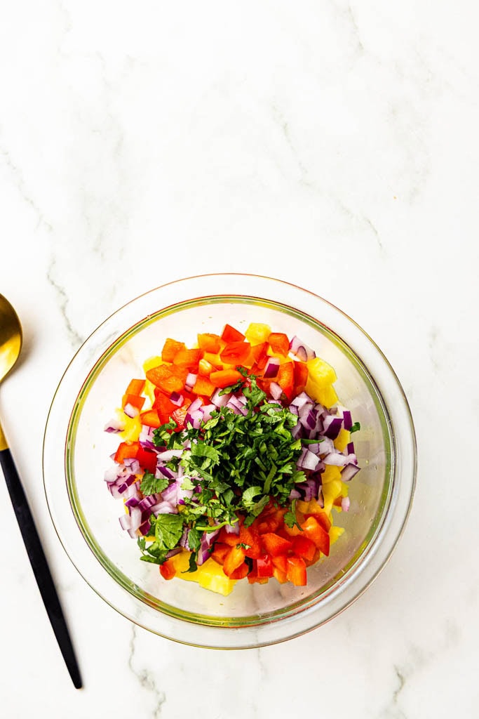 glass bowl containing fruits and veggies with cilantro on top with spoon on side